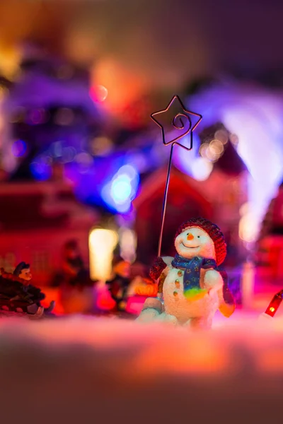 Kind spielt mit Schneemann im bunten Weihnachtsdorf auf Schnee. — Stockfoto