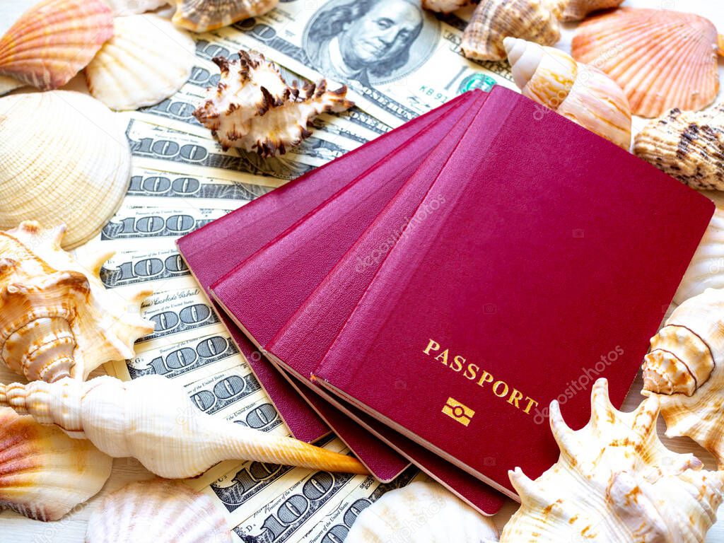 Four passports on a fan of hundred-dollar bills surrounded by sea shells