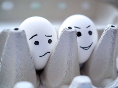 İki tavuk yumurtası bir kutuda oturur. Biri üzgün, diğeri ise gülen suratlı.