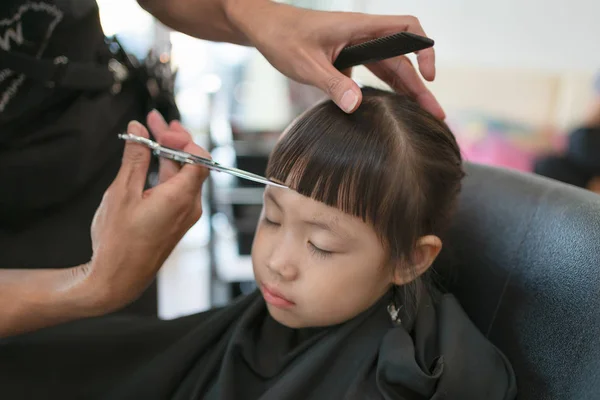 Little girl getting haircut by hairdresser at the barbershop. — Stock Photo, Image