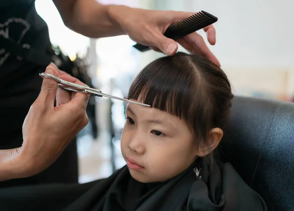 Little girl getting haircut by hairdresser at the barbershop.