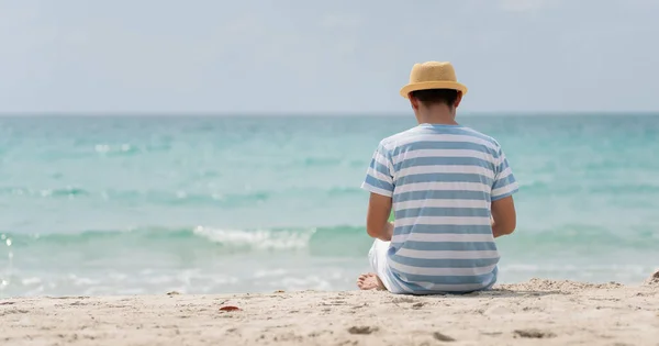 Πίσω όψη ενός Ασιάτη που κάνει διακοπές φορώντας καπέλο καθισμένος στην παραλία — Φωτογραφία Αρχείου