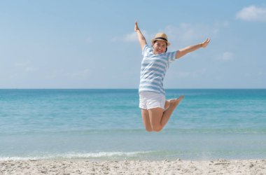 Şapka takan Asyalı genç kadın sahilde neşe ve mutlulukla zıplıyor..