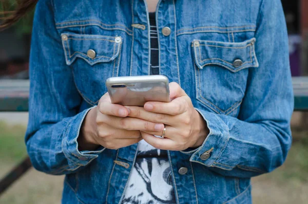 Menina em jeans jaqueta usando telefone inteligente — Fotografia de Stock