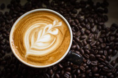 Kahve çekirdeklerine karşı kırmızı bardakta sıcak latte sanatı