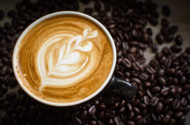 Kahve çekirdeklerine karşı kırmızı bardakta sıcak latte sanatı