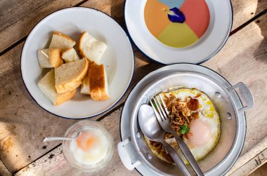 Kahvaltı seti: Buharda krema, buğulanmış ekmek, tavada yumurta ve ahşap masada kaynamış yumurta.