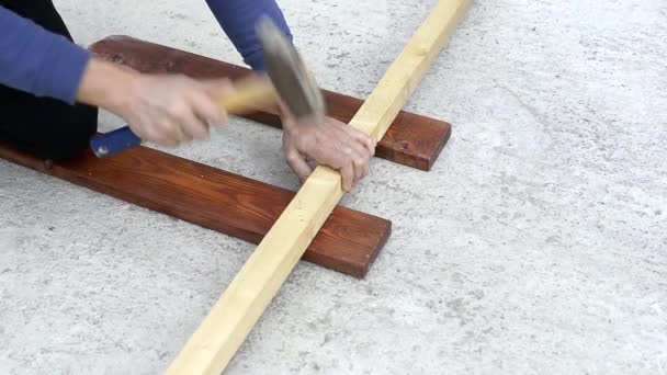 Arbetare hamrar metallspikar i en bräda — Stockvideo