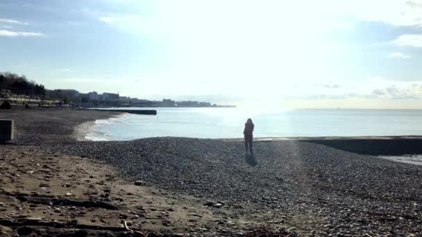 La ragazza con il cappotto rosso che corre sul mare godendo dei raggi del sole — Video Stock
