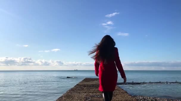 La ragazza col cappotto rosso che corre intorno al frangiflutti — Video Stock