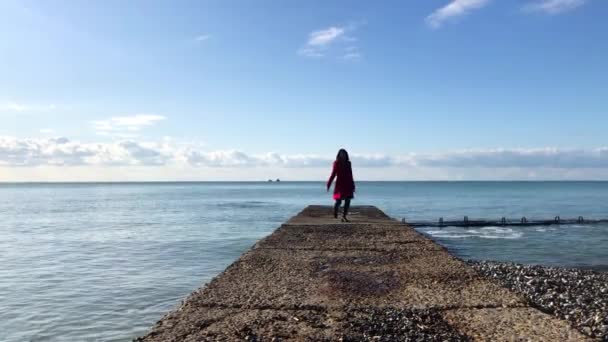 La ragazza col cappotto rosso che corre intorno al frangiflutti — Video Stock