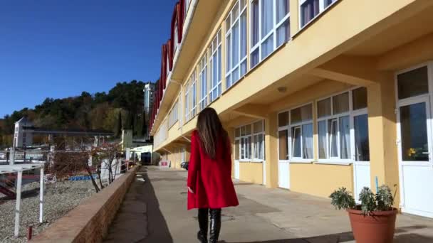 La ragazza con il cappotto rosso cammina sulla spiaggia con un bel tempo soleggiato — Video Stock