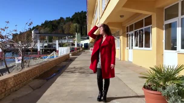 La chica con el abrigo rojo camina por la playa en claro tiempo soleado — Vídeo de stock
