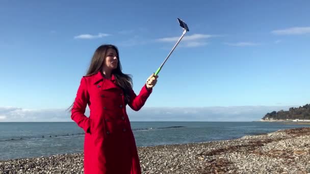 Selfie çubuğu olan bir kadın deniz kenarında yürüyor, blog için bir video kaydediyor. — Stok video