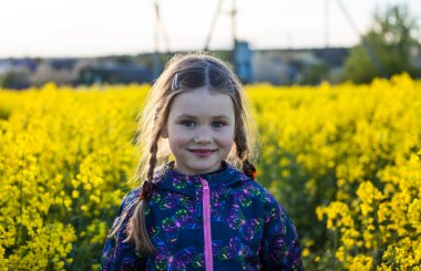 Çiçek açan kolza tohumu tarlasında yürüyen küçük tatlı kız, kırsal cennet manzarası.