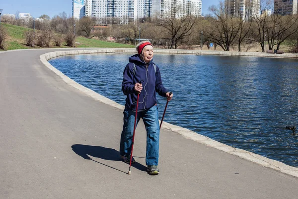 Popular sport around the world-Nordic walking. an elderly woman goes to the spring Park . Active people on the street.