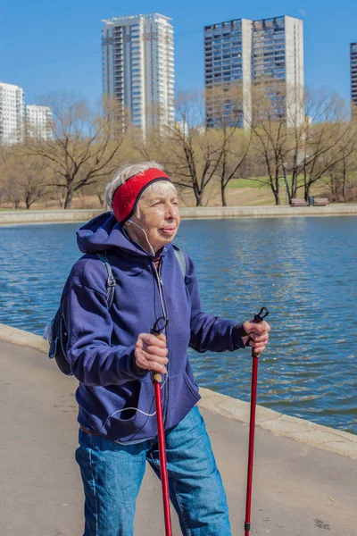 Popular sport around the world-Nordic walking. an elderly woman goes with a backpack to the spring Park . Active people on the street. senior woman walking actively.