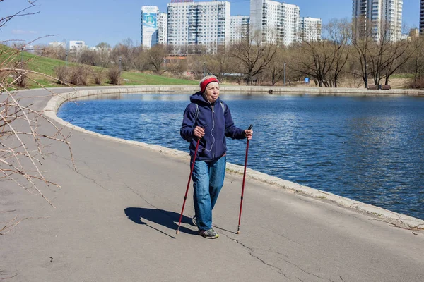 Popular sport around the world-Nordic walking. an elderly woman goes with a backpack to the spring Park . Active people on the street. senior woman walking actively.