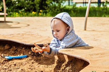 Şirin yürümeye başlayan çocuk bahçesi kum havuzunda bahar güneşli bir günde oynamaya. Akıllı neşeli çocuk bir yürüyüş.