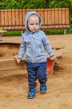 Şirin yürümeye başlayan çocuk bahçesi kum havuzunda bahar güneşli bir günde oynamaya. Akıllı neşeli çocuk bir yürüyüş.