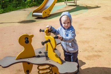 Şirin yürümeye başlayan çocuk bahçesi kum havuzunda bahar güneşli bir günde oynamaya. Akıllı neşeli çocuk bir yürüyüş. komik çocuk salıncakta oturan.