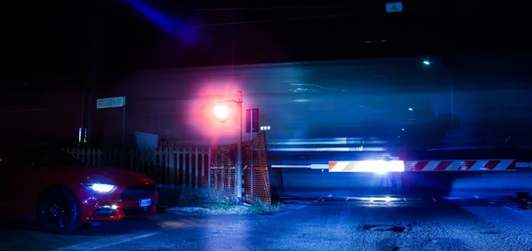 Järnvägen passerar i natt med passerande tåg och bil — Stockfoto