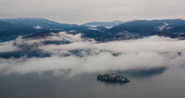 Città di montagna vicino al grande lago circondato da nebbia e nuvole — Foto Stock