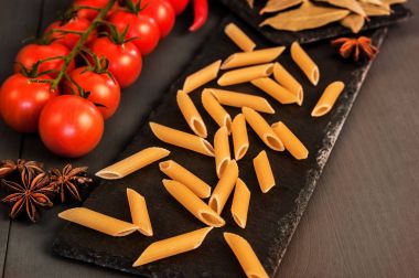 Makarna domates ve biber gri bir arka plan üzerinde siyah bir gemide