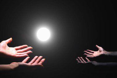 Yaşayan ve ölü eller siyah arka planda ışığa uzanır.