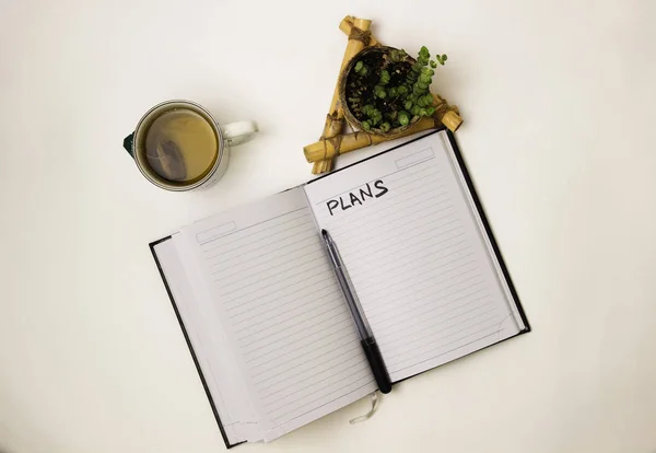 a cup of tea, a notebook and a flower, plans, on a white backgro