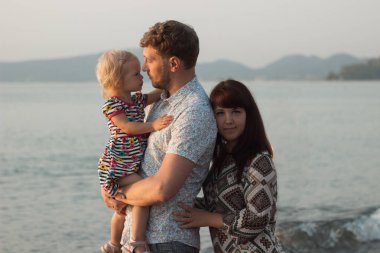 Anne, baba ve kızı. Baba bir kızı onun kollarında tutar, annesi kızı görünüyor. Deniz. Mutluluk. Şafak.