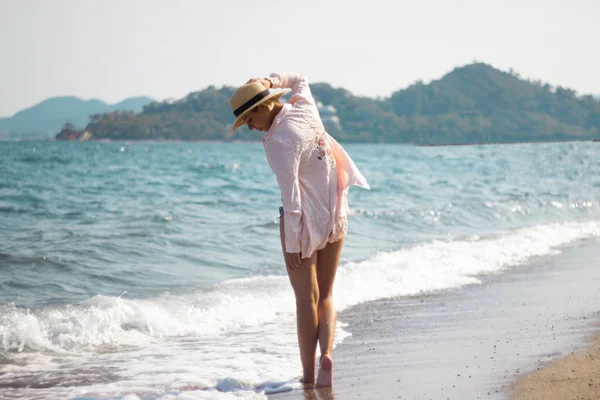 Een jong meisje in een bleke roze shirt en een stro hoed wandelen langs — Stockfoto
