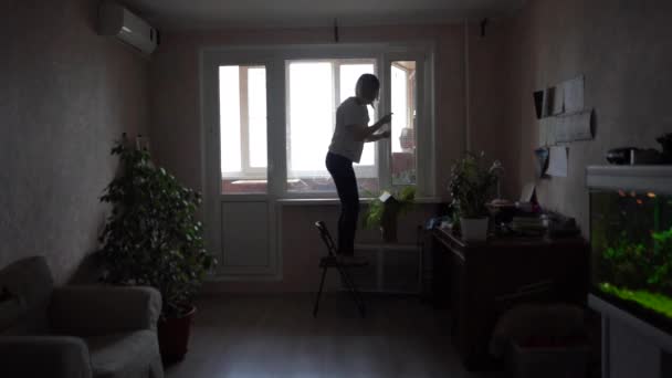En kvinna tar bort krukväxter från ett fönster och tvättar ett fönster. Ett barn springer bredvid henne. Snabbare skottlossning — Stockvideo