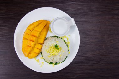 Hindistancevizi sütlü taze mangolu yapış yapış pilav kahverengi ahşap masaya beyaz tabak koymak Tayland usulü tropikal tatlıdır. Üst görünüm.