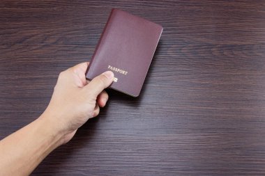 Kahverengi ahşap masada uluslararası pasaport tutan bir adam..