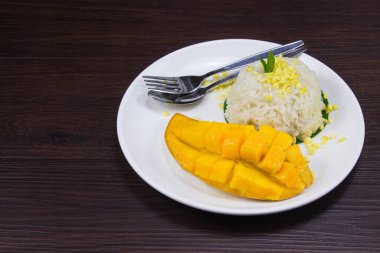 Yapışkan pirinç taze olgun mango ve hindistan cevizi sütü. Kahverengi ahşap masaya beyaz tabak koy. Tayland usulü tropikal tatlı..