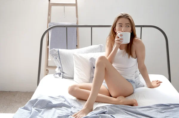 Žena sedí v posteli s nápojem — Stock fotografie