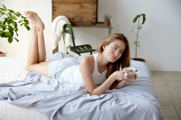 Yatakta yatan ve kahve içme kadın — Stok fotoğraf