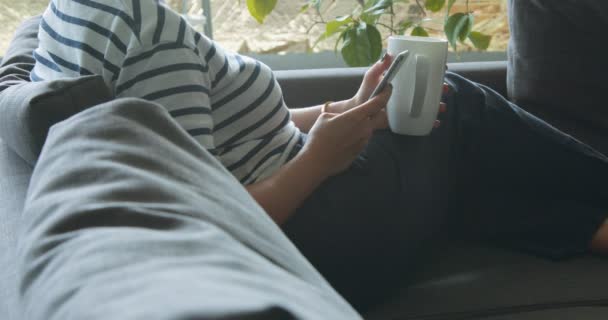 La mujer con la taza y el smartphone descansa en el sofá — Vídeo de stock