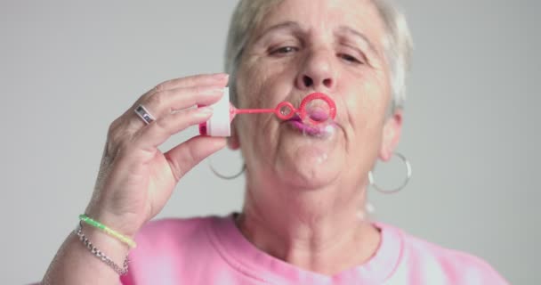 Bejaarde vrouw klap bubbles om camera — Stockvideo