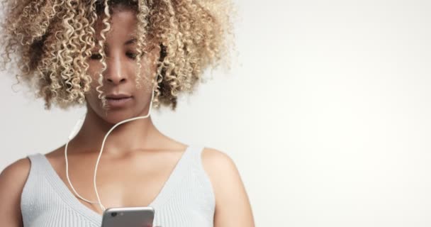 Portrait de beauté mixte femme aux cheveux afro et taches de rousseur avec écouteurs et smartphone — Video