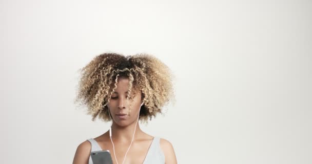 Portrait de beauté mixte femme aux cheveux afro et taches de rousseur avec écouteurs et smartphone — Video