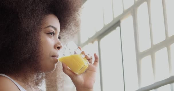 Negro mujer con enorme afro cabello bebe un jugo de naranja — Vídeos de Stock