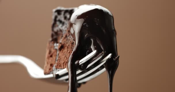 Piece of chocolate cake on a fork closeup with slow liquid toping pouring on — Stock Video