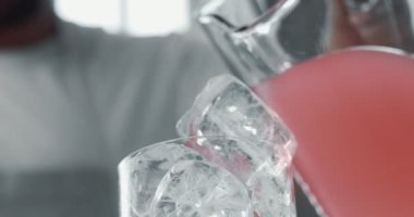 closeup of cubes of ice in glass and a pink lemonade pouring on it