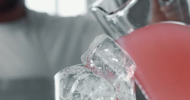 Primer plano de cubos de hielo en vidrio y una limonada rosa vertiendo sobre ella — Vídeo de stock