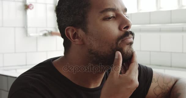Человек смешанной расы касается его лица и бороды перед бритьем — стоковое видео
