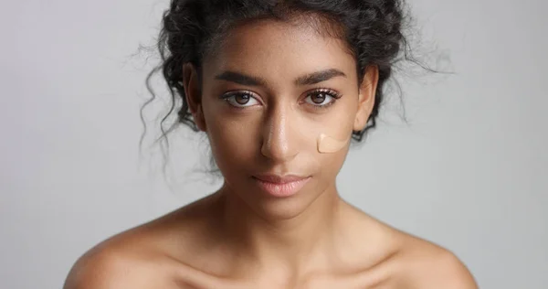 Junge Frau aus dem Mittleren Osten im Studio mit einem Fundament auf der Wange Nahaufnahme, die die Haut berührt — Stockfoto