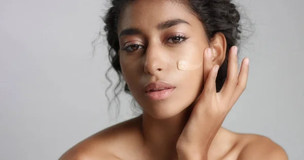 Junge Frau aus dem Mittleren Osten im Studio mit einem Fundament auf der Wange Nahaufnahme, die die Haut berührt — Stockfoto