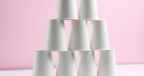 Torre hecha de tazas de papel blanco sobre fondo rosa — Vídeos de Stock